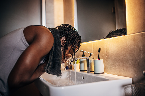Un hombre, un apuesto hombre negro que se lava la cara en el baño por la mañana.